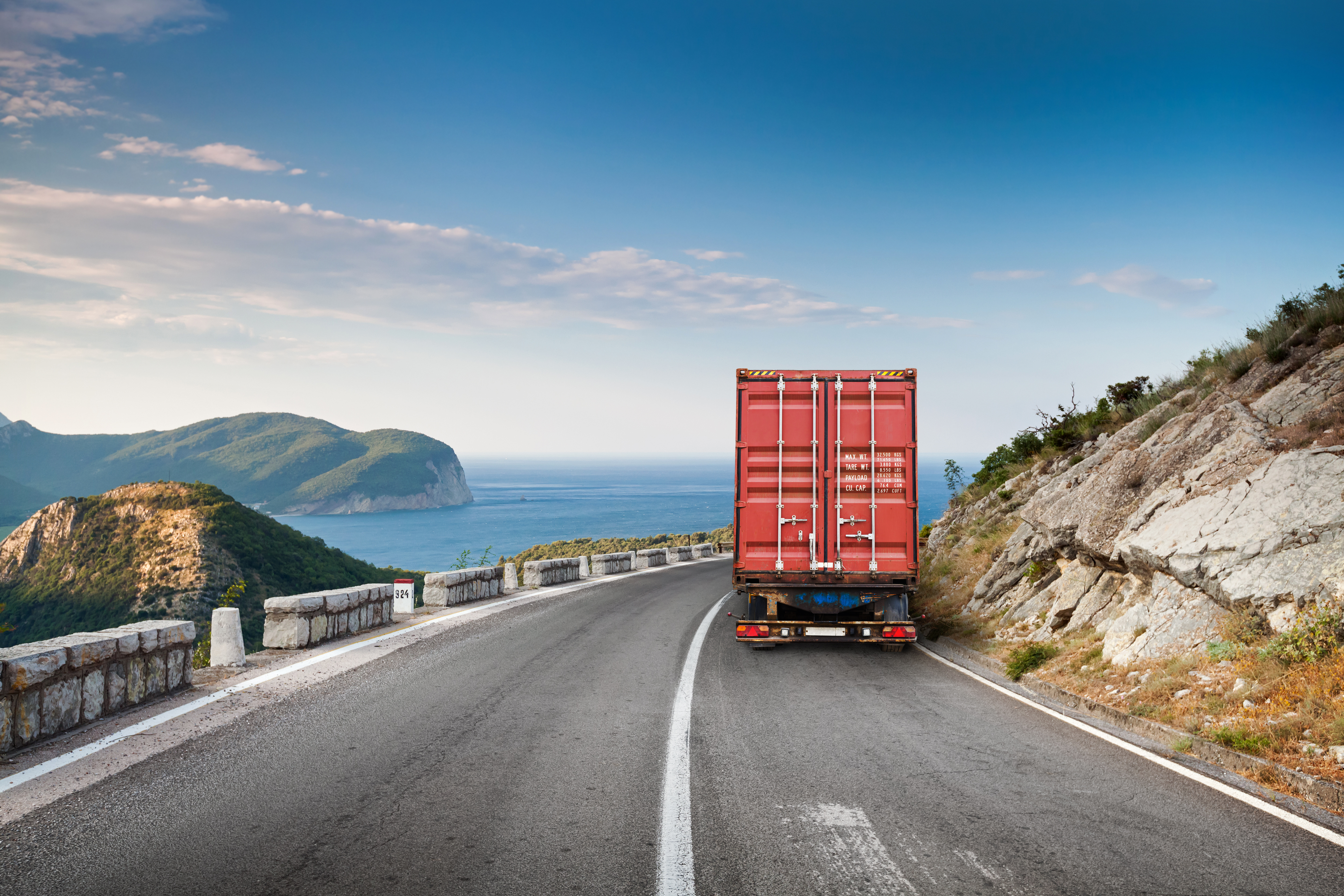 A single truck driving around a bend with ocean in the background